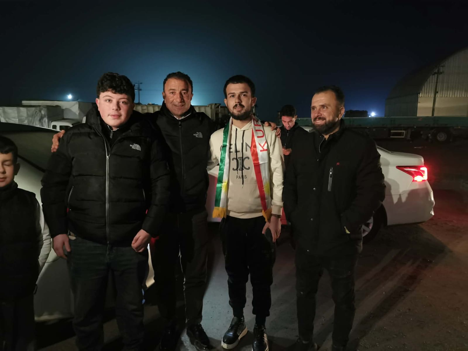 Association members welcoming a returned migrant at the border crossing, wearing the Kurdish flag.